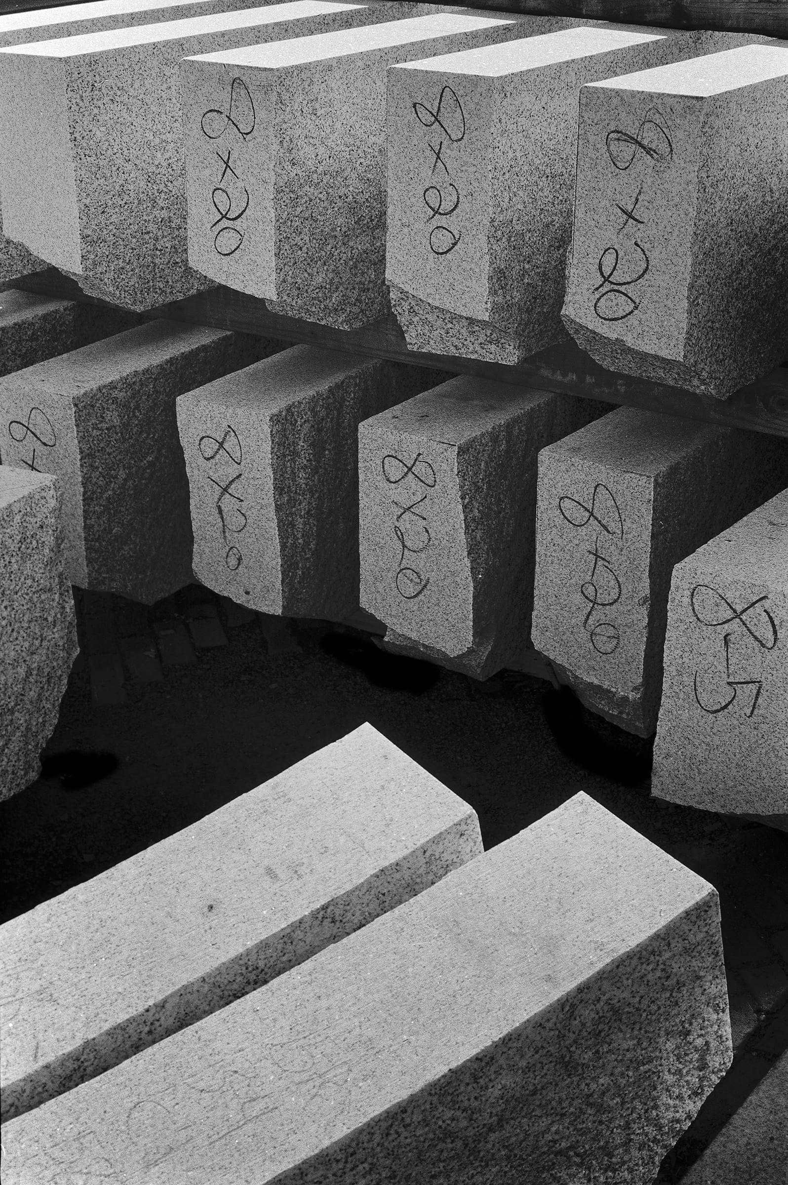 Stacked cut stone blocks marked 8x20 in black marker, in hard sunlight