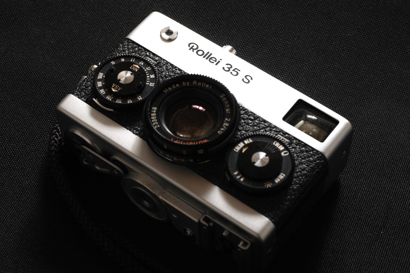 Silver-and-black Rollei 35 S camera viewed from above on black fabric.